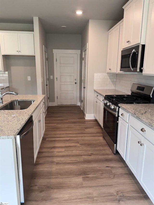 kitchen featuring appliances with stainless steel finishes, white cabinetry, wood-type flooring, sink, and light stone counters