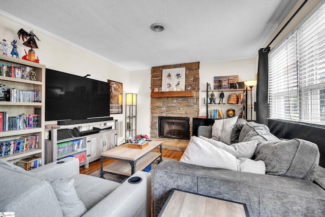 living room with hardwood / wood-style flooring, a textured ceiling, a stone fireplace, and crown molding