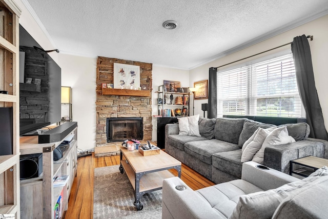 living room with a stone fireplace, crown molding, a textured ceiling, and light hardwood / wood-style floors