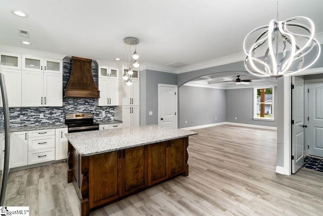 kitchen with arched walkways, decorative backsplash, a kitchen island, custom exhaust hood, and stainless steel range with electric cooktop