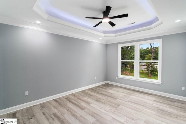 empty room featuring a raised ceiling, visible vents, light wood finished floors, and baseboards