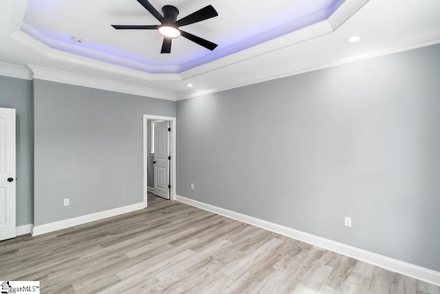 empty room with light wood finished floors, baseboards, a raised ceiling, a ceiling fan, and crown molding