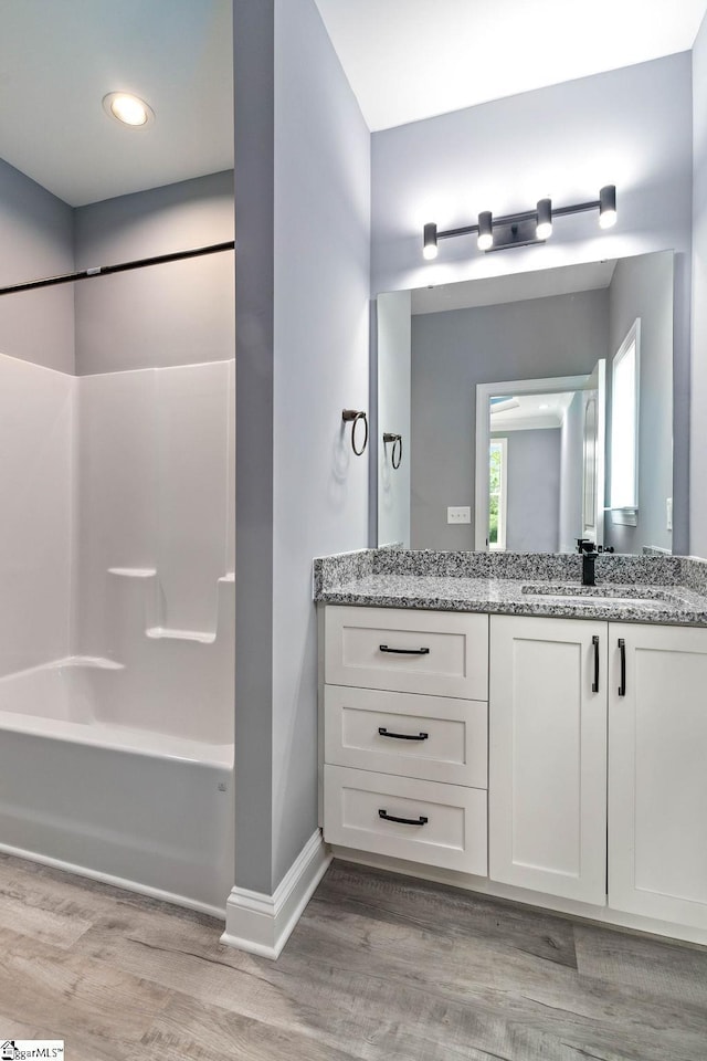 full bath featuring tub / shower combination, vanity, baseboards, and wood finished floors