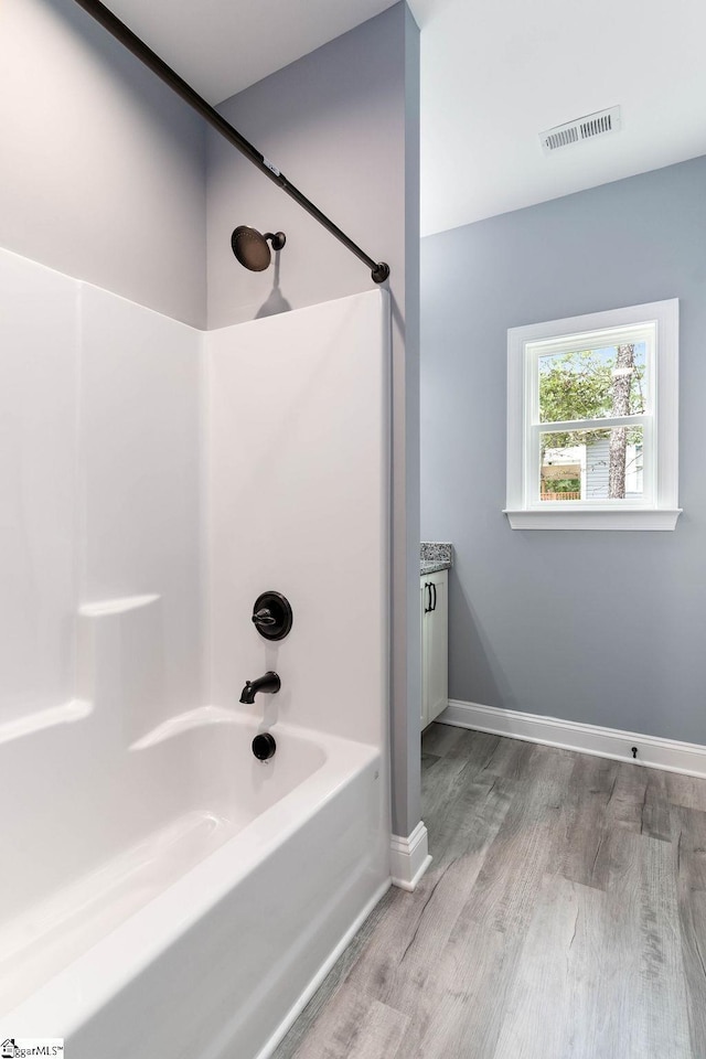 full bathroom with bathing tub / shower combination, wood finished floors, visible vents, and baseboards