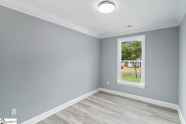 empty room featuring crown molding, light wood-type flooring, visible vents, and baseboards