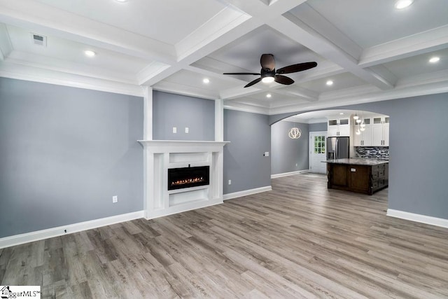 unfurnished living room with light wood-type flooring, a warm lit fireplace, baseboards, and beam ceiling