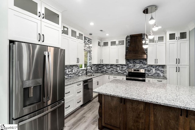 kitchen featuring backsplash, appliances with stainless steel finishes, white cabinetry, a sink, and premium range hood