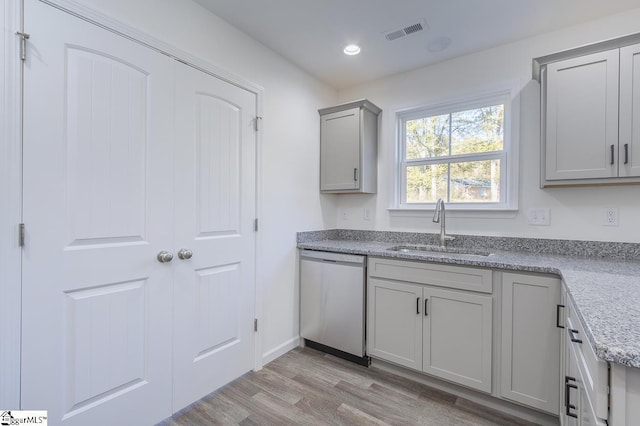 kitchen with sink, stainless steel dishwasher, gray cabinets, light wood-type flooring, and light stone counters