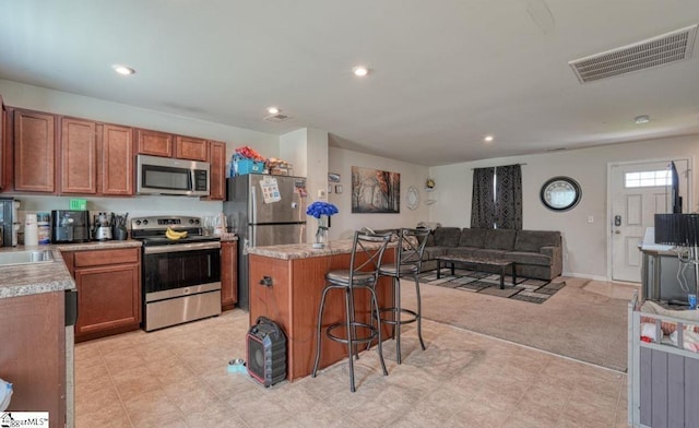 kitchen with light countertops, a kitchen breakfast bar, appliances with stainless steel finishes, open floor plan, and visible vents