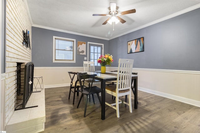 dining room with a brick fireplace, crown molding, dark hardwood / wood-style floors, and ceiling fan