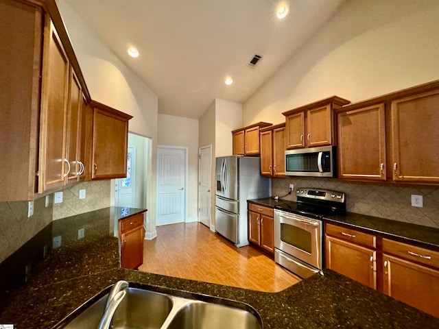 kitchen featuring dark stone counters, stainless steel appliances, light hardwood / wood-style flooring, and tasteful backsplash