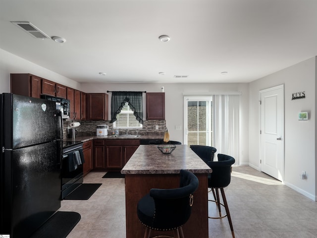 kitchen with light tile patterned flooring, black appliances, tasteful backsplash, and a center island