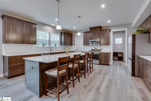 kitchen with stainless steel appliances, light hardwood / wood-style floors, backsplash, and a center island