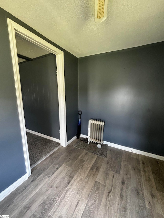 unfurnished room featuring wood-type flooring, radiator, and a textured ceiling