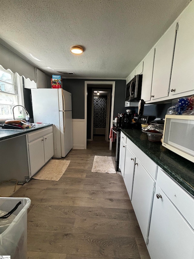 kitchen with white cabinets, wood-type flooring, white appliances, and a textured ceiling