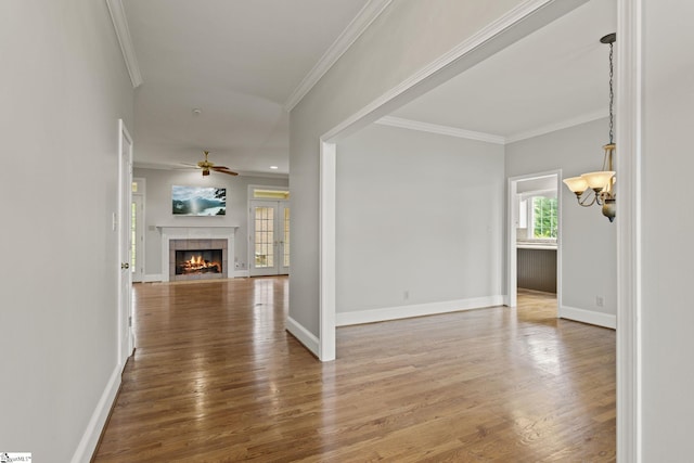 interior space with a tile fireplace, crown molding, wood-type flooring, and ceiling fan with notable chandelier