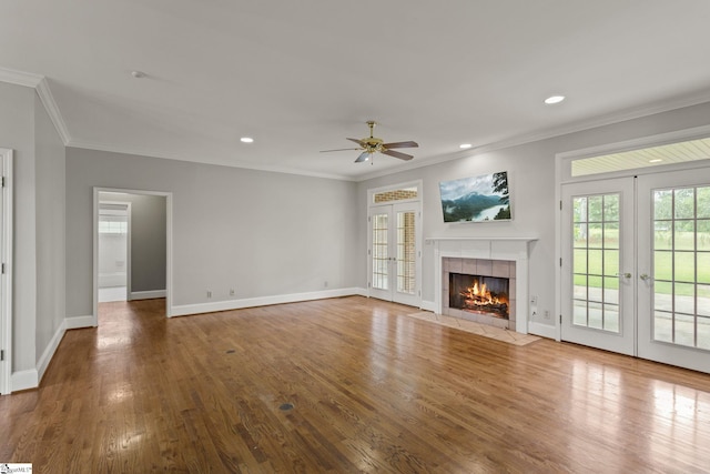 unfurnished living room with french doors, a tile fireplace, ornamental molding, hardwood / wood-style flooring, and ceiling fan