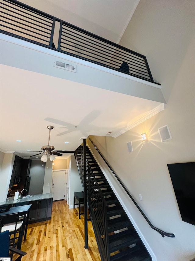 staircase featuring light wood-type flooring, ornamental molding, and ceiling fan