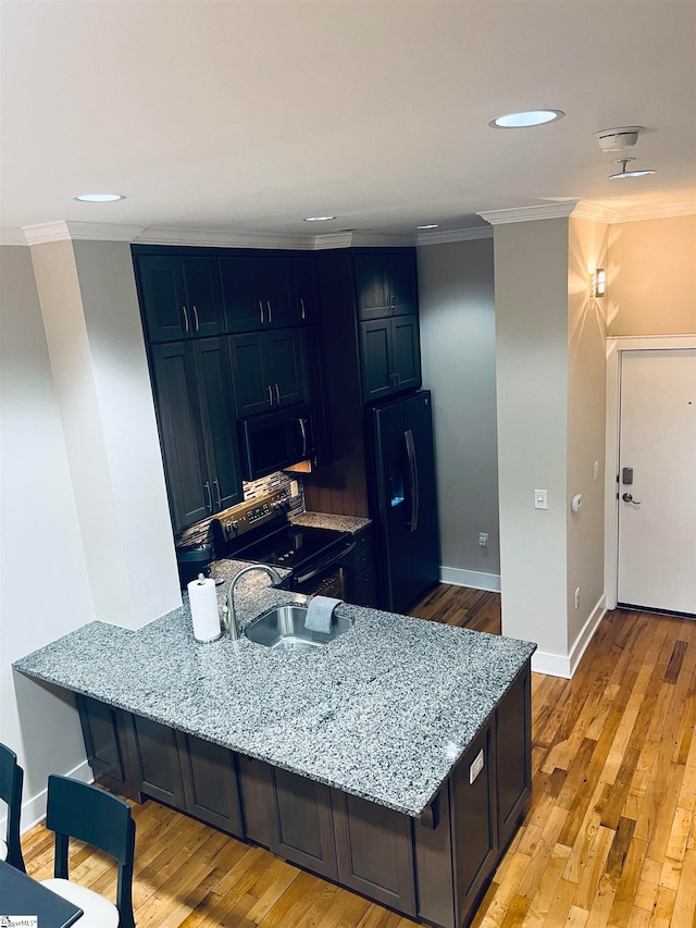 kitchen with light wood-type flooring, sink, ornamental molding, black appliances, and light stone counters