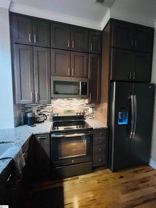 kitchen with tasteful backsplash, dark brown cabinets, stainless steel appliances, light hardwood / wood-style floors, and light stone counters