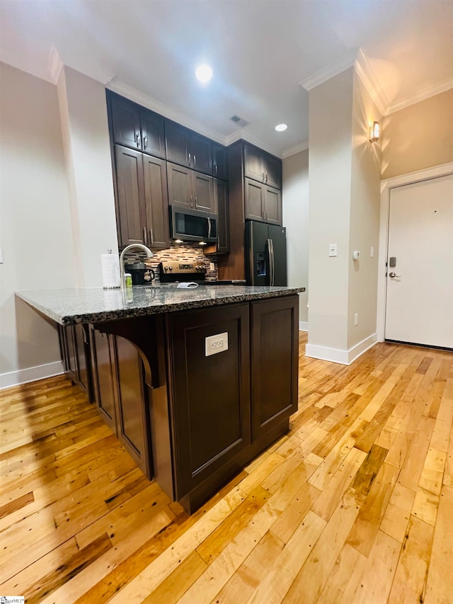 kitchen with appliances with stainless steel finishes, kitchen peninsula, dark stone counters, and light hardwood / wood-style floors