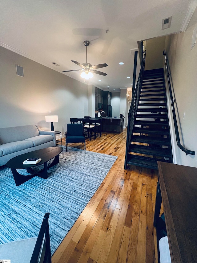 living room with light hardwood / wood-style flooring, ornamental molding, and ceiling fan