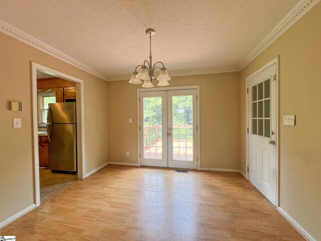 unfurnished dining area with light wood-type flooring, ornamental molding, a textured ceiling, and an inviting chandelier