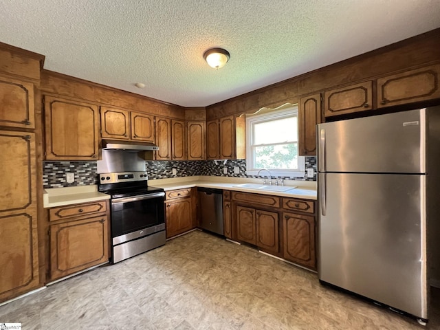 kitchen with under cabinet range hood, light countertops, appliances with stainless steel finishes, and a sink