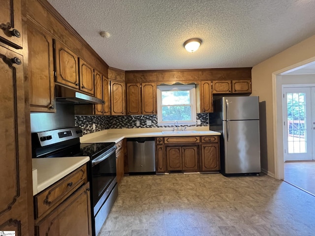 kitchen with a sink, decorative backsplash, light countertops, stainless steel appliances, and under cabinet range hood