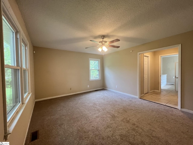 carpeted empty room with a textured ceiling, baseboards, visible vents, and ceiling fan