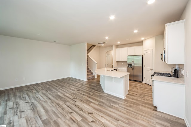 kitchen with light hardwood / wood-style flooring, white cabinets, a center island with sink, stainless steel appliances, and sink