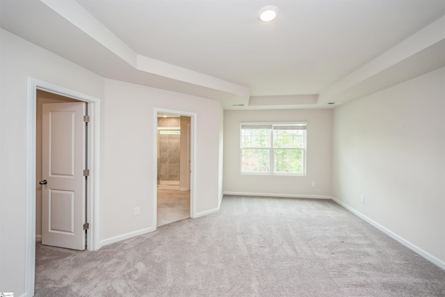 interior space featuring connected bathroom, light colored carpet, and a raised ceiling