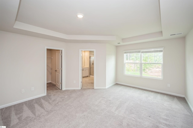 unfurnished bedroom with a spacious closet, ensuite bath, light colored carpet, and a tray ceiling