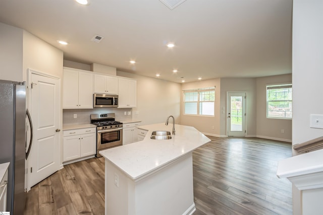 kitchen featuring light wood-type flooring, appliances with stainless steel finishes, an island with sink, backsplash, and sink