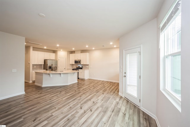 kitchen with white cabinets, a center island with sink, light wood-type flooring, stainless steel appliances, and sink