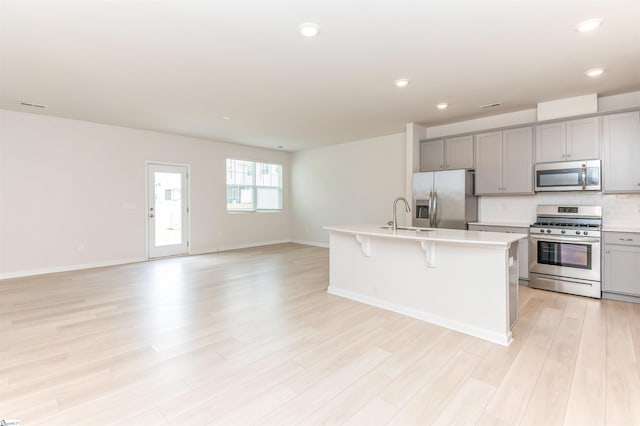 kitchen featuring an island with sink, stainless steel appliances, light hardwood / wood-style floors, and gray cabinets