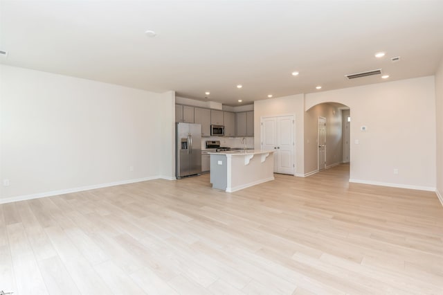 kitchen with a kitchen island with sink, appliances with stainless steel finishes, light wood-type flooring, sink, and gray cabinetry