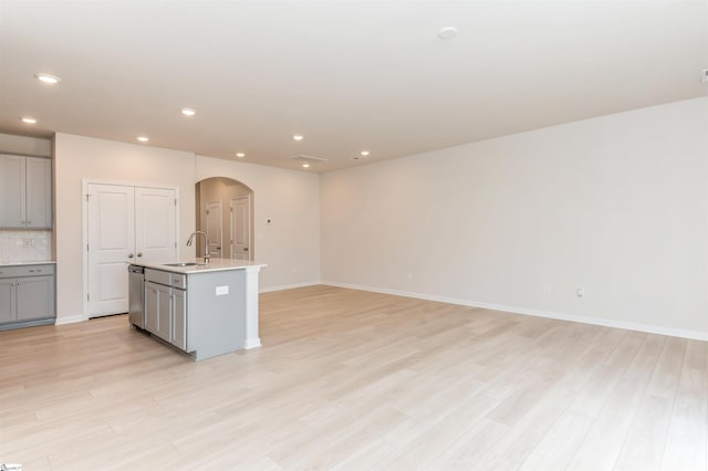 kitchen with light wood-type flooring, a center island with sink, sink, tasteful backsplash, and gray cabinetry