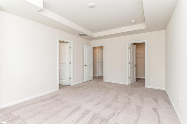 unfurnished bedroom with a closet, a raised ceiling, a walk in closet, and light colored carpet