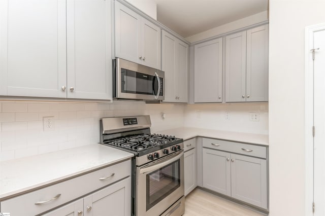 kitchen with gray cabinetry, light hardwood / wood-style flooring, stainless steel appliances, and backsplash