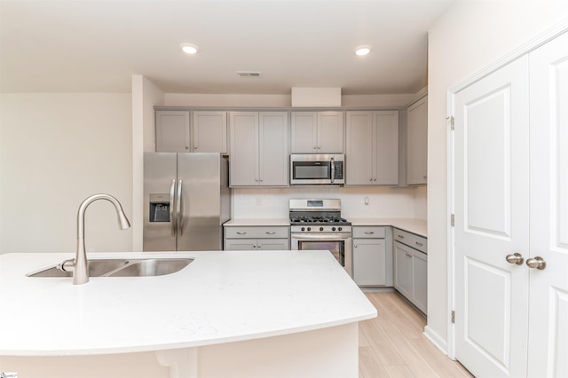 kitchen with decorative backsplash, stainless steel appliances, gray cabinetry, light hardwood / wood-style flooring, and sink