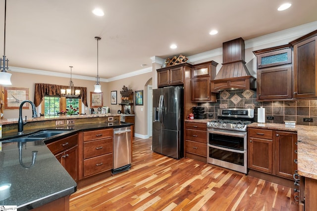 kitchen featuring sink, premium range hood, dark stone countertops, hanging light fixtures, and stainless steel appliances