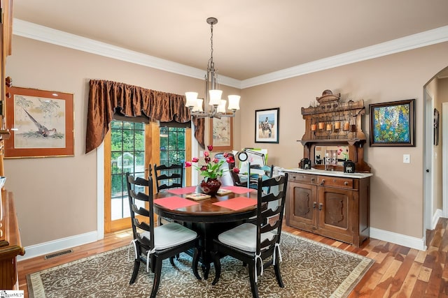 dining space featuring ornamental molding, a notable chandelier, and light hardwood / wood-style flooring