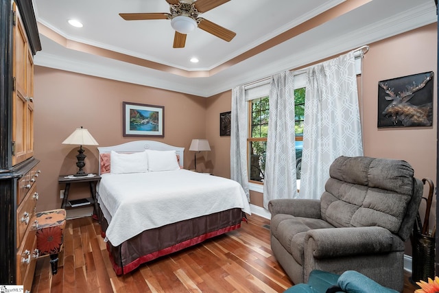 bedroom with crown molding, dark hardwood / wood-style floors, ceiling fan, and a tray ceiling