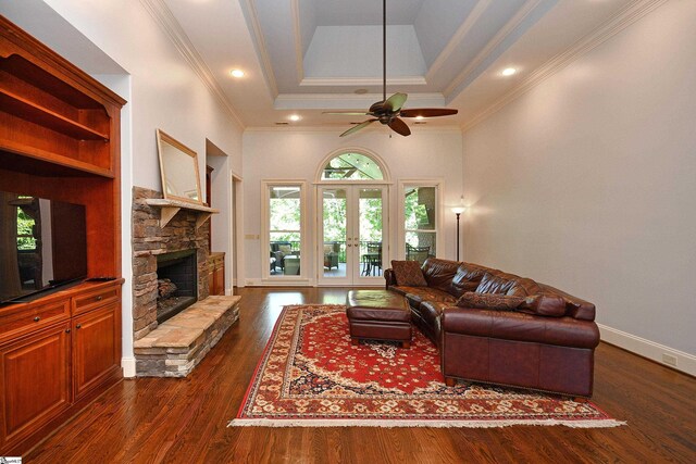 living room with dark hardwood / wood-style floors, ceiling fan, a raised ceiling, a stone fireplace, and french doors