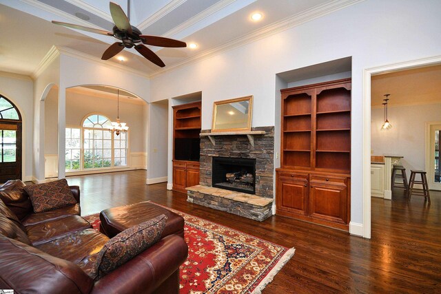 living room with ceiling fan with notable chandelier, a fireplace, ornamental molding, and dark wood-type flooring