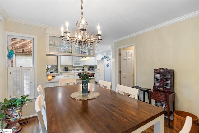 dining space with sink, ornamental molding, hardwood / wood-style flooring, and an inviting chandelier