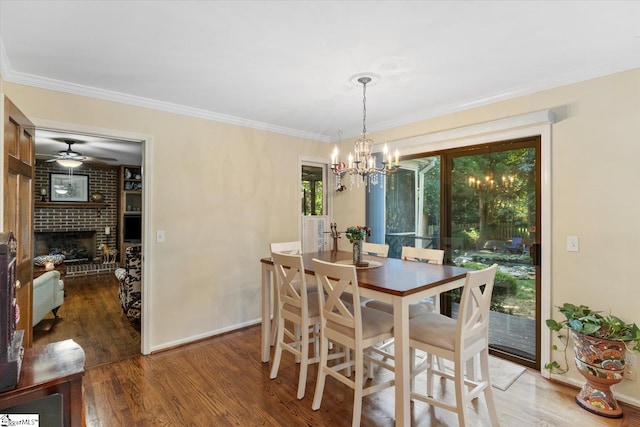 dining space featuring ceiling fan with notable chandelier, hardwood / wood-style floors, brick wall, a fireplace, and ornamental molding