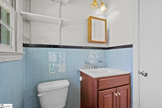 half bathroom with tile walls, wainscoting, vanity, and toilet