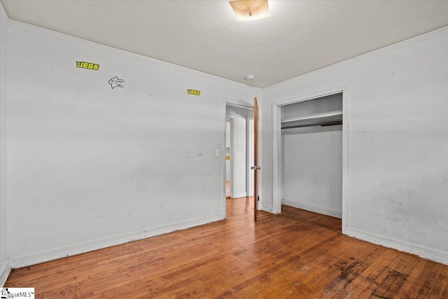 unfurnished bedroom with crown molding, a closet, baseboards, and hardwood / wood-style floors